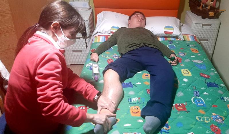 Fisioterapeuta realizando tratamiento aún niño tumbado en la cama de su habitación