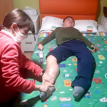 Fisioterapeuta realizando tratamiento aún niño tumbado en la cama de su habitación