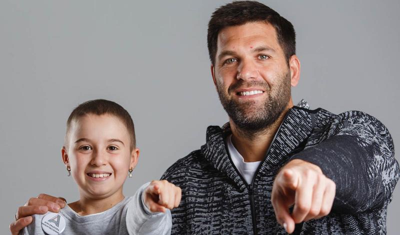 Felipe Reyes (ex jugador de baloncesto) junto a un niño sonríen y señalan al observador de la foto, se lee ¡ Graicas! y Aceleradora Unoentrecienmil debajo de una A mayúscula de colores, y en la parte inferior de la foto la web www.aceleradoraunoentrecienmil.org