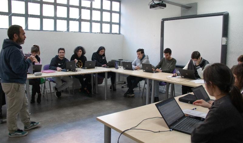 Imagen de un aula en la que se encuentra un profesor dando clase a un grupo de chicos y chicas