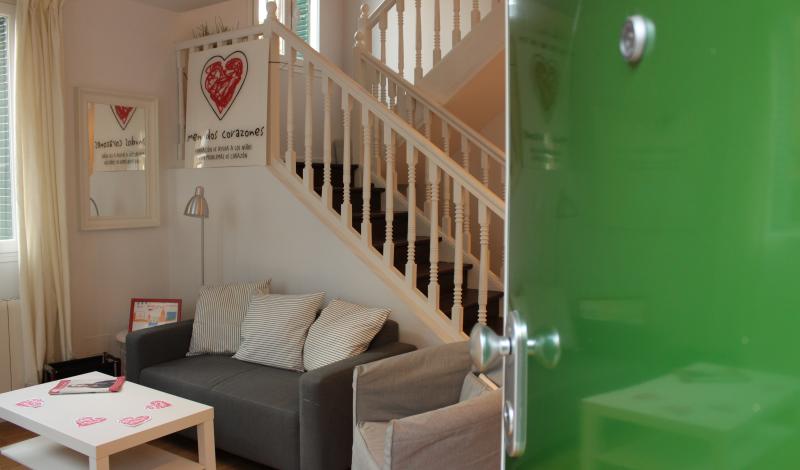 Es una recepcion de una casa para familias, con un sofa y una mesa blanca y el logo de menudos corazones.