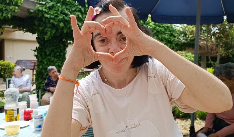 Una persona hace una forma de corazón con sus manos con un jardín de fondo en un picnic