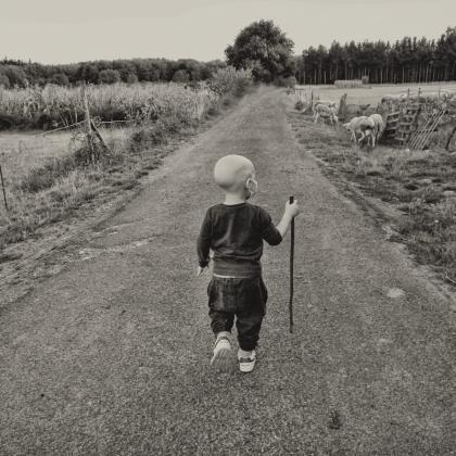 En la imagen aparece un niño de espaldas de unos seis años, que ha perdido el pelo, caminando hacia adelante apoyándose en un palo.