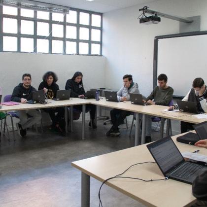 Imagen de un aula en la que se encuentra un profesor dando clase a un grupo de chicos y chicas