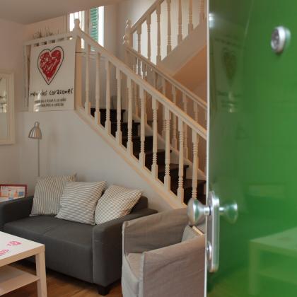 Es una recepcion de una casa para familias, con un sofa y una mesa blanca y el logo de menudos corazones.