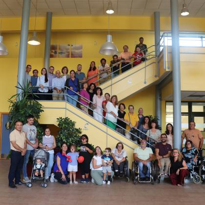 Grupo de personas de la asociación de osteogénesis imperfecta reunidas en un vestíbulo amplio, posando frente a unas escaleras.