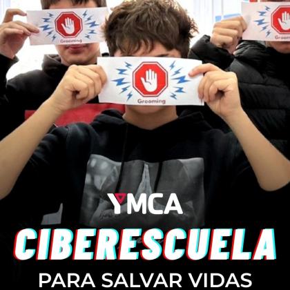 En la imagen aparecen varios menores en situación de vulnerabilidad social participando en una actividad de sensibilización. Cada uno sostiene una tarjeta rectangular con el símbolo de “Grooming”, representado por una mano levantada dentro de un hexágono rojo, acompañada de líneas azules que simulan una alerta. Se encuentran en un espacio interior iluminado, probablemente un aula o sala de actividades. En la parte inferior de la imagen se muestra el logotipo de YMCA, seguido del título  “CIBERESCUELA"